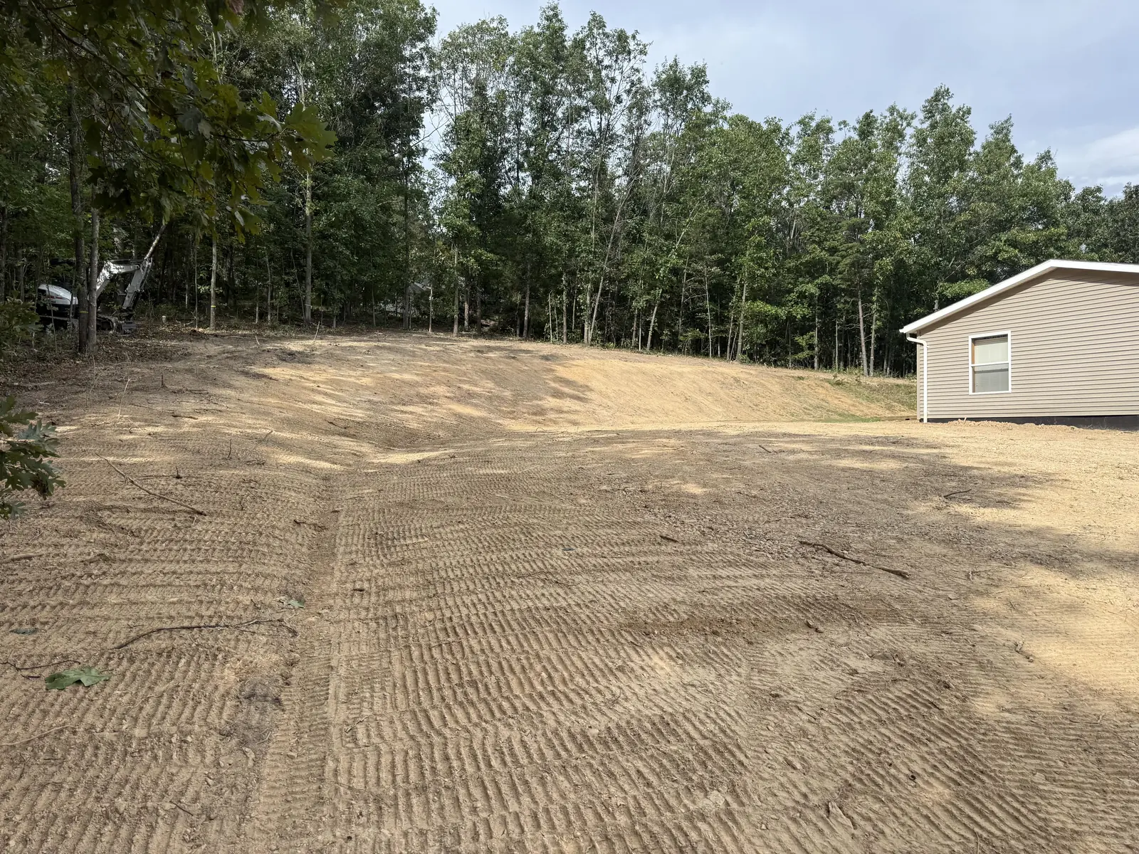 Freshly graded yard and bank behind a home, mini excavator parked at the tree line