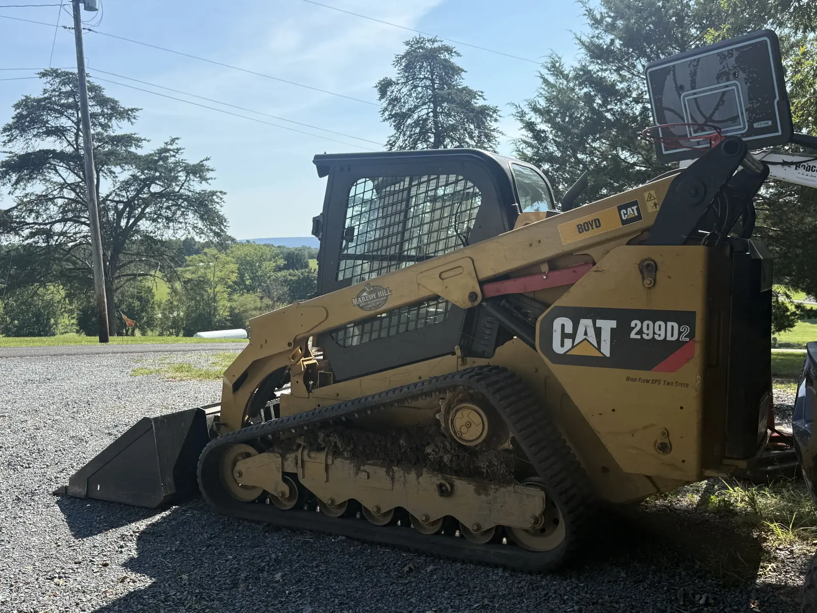 Tracked skid steer with a bucket parked on gravel, ridges in the distance