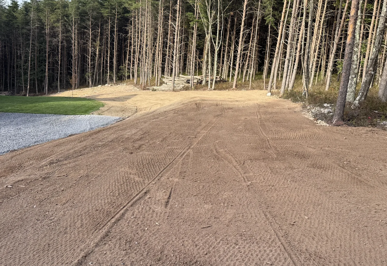 Before: fresh topsoil spread and graded beside a gravel drive, track marks across it